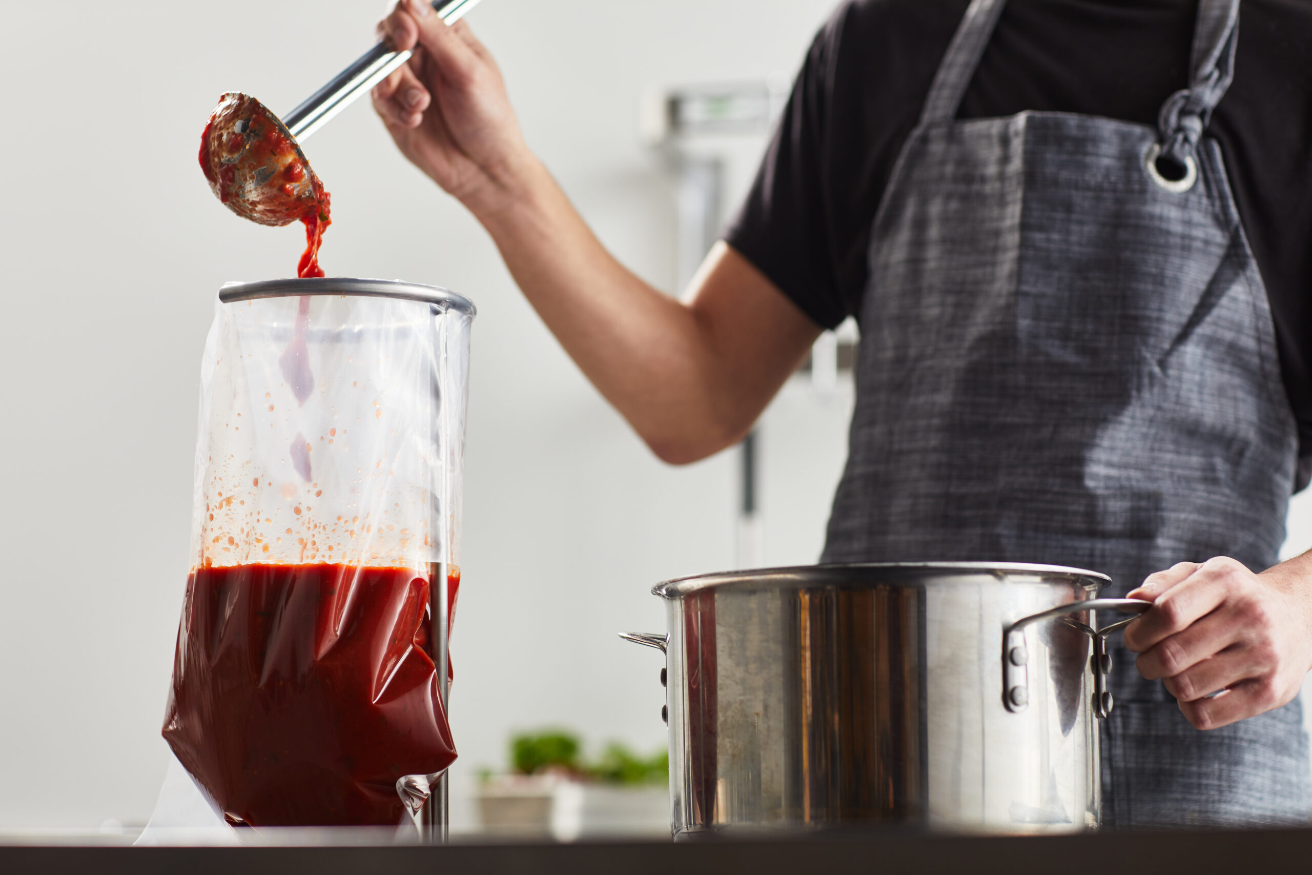 Chill bag filled with marinara sauce, supported by a ring stand and funnel for safe storage and reheating.