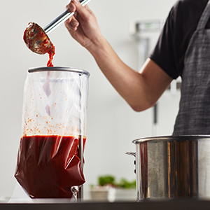 Chill bag filled with marinara sauce, supported by a ring stand and funnel for safe storage and reheating.